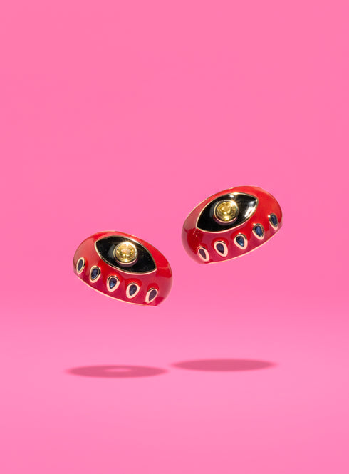 Two Evil Eye Signet Rings — both red — side by side on a pastel pink surface. Each ring features a gold-plated band, enamel finish, and zircon evil eye design. Ideal for statement jewelry collectors and alternative fashion enthusiasts.