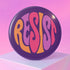 Close-up of a glossy, round purple pinback button. The button features the word "RESIST" in a bold, 70s-style psychedelic font that fills the entire surface. The bubbly, wavy letters alternate in color between a vibrant orange, a light peach-pink, and a deep magenta, creating a powerful and retro statement piece. The design has a distinct groovy and feminist protest aesthetic, making it a perfect accessory for jackets, bags, or activist apparel.