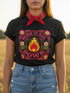 A high-resolution product image of a black unisex t-shirt featuring the ‘BURN IT ALL DOWN’ design in a folk-art style. The central motif is a vibrant orange and yellow flame surrounded by a circular medallion and a square floral border with red and pink flowers, white daisies, and green leaves. The print uses a faux-embroidery technique to create a trompe-l’œil 3D texture on a smooth 2D surface. The shirt has a ribbed knit collar, set against a high-contrast background.