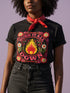 A high-resolution product image of a black unisex t-shirt featuring the ‘BURN IT ALL DOWN’ design in a folk-art style. The central motif is a vibrant orange and yellow flame surrounded by a circular medallion and a square floral border with red and pink flowers, white daisies, and green leaves. The print uses a faux-embroidery technique to create a trompe-l’œil 3D texture on a smooth 2D surface. The shirt has a ribbed knit collar, set against a high-contrast background.