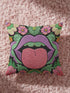 A square decorative pillow cover featuring a flat print design that mimics textured embroidery. The bold motif is set on a solid black background and centers on a pair of large, light purple lips with a bright pink, textured-looking tongue sticking out. Green ruffled leaves outline the mouth, and stylized pink daisy-like flowers sit at the top corners and bottom edges. The fabric has a faux linen weave texture, presenting a vibrant, symmetrical, and maximalist pop art aesthetic.