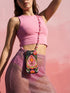 Black phone case featuring a faux embroidery style print with a central pink planchette design. The planchette contains a single eye motif and a circular sun element above it. Surrounding the design are orange, red, and pink flowers, green leaves, small cream stars, and crescent moons. The print creates a stitched textile illusion on a smooth matte protective case with dual layer construction.