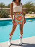 A vibrant bodycon mini skirt featuring a structured grid of retro geometric medallions. The pattern includes concentric circles in red, yellow, and blue, stylized daisy flower motifs, and red and white checkered squares. The skirt has a high-waist elastic band and a smooth, matte performance knit texture. The background is a neutral off-white. This maximalist design utilizes saturated primary colors to create a 70s-inspired psychedelic aesthetic. No purple or navy is present in the print.