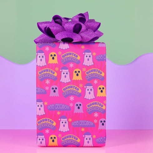 Bright pink christmas wrapping paper covered in cute ghost characters wearing Santa hats, with "Haunted Holiday" and "Boo Humbug" text, and snowflake accents.