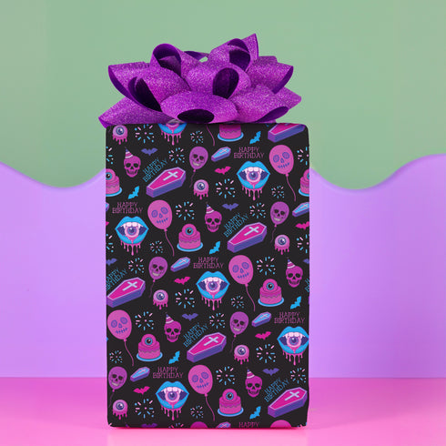 Spooky birthday wrapping paper with neon pink skulls, blue coffins, eyeballs, and bats on black background. Vibrant and gothic design for unique gift presentation.