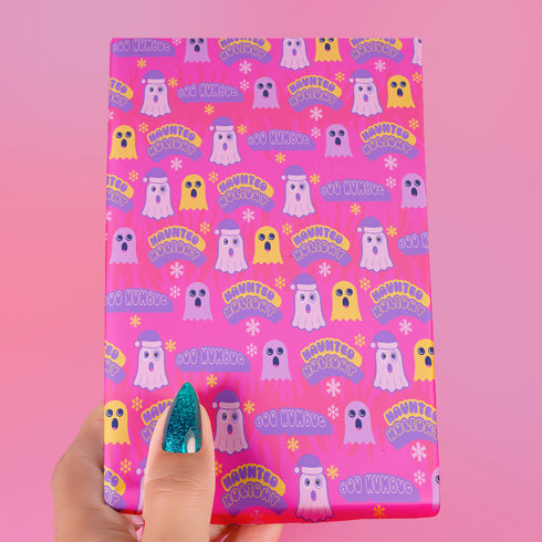 Bright pink christmas wrapping paper covered in cute ghost characters wearing Santa hats, with "Haunted Holiday" and "Boo Humbug" text, and snowflake accents.