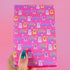 Bright pink christmas wrapping paper covered in cute ghost characters wearing Santa hats, with "Haunted Holiday" and "Boo Humbug" text, and snowflake accents.