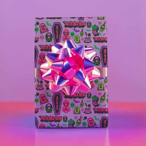 Vibrant purple wrapping paper with gothic-inspired design for 50th birthdays. Features colorful skulls wearing party hats, coffins, 'RIP 40s' tombstones, and 'Youth Dies Here' text. Perfect for edgy, humorous gifts to 50-year-olds.