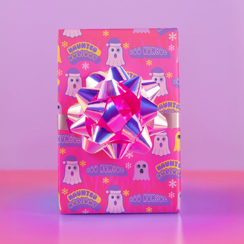 Bright pink christmas wrapping paper covered in cute ghost characters wearing Santa hats, with "Haunted Holiday" and "Boo Humbug" text, and snowflake accents.