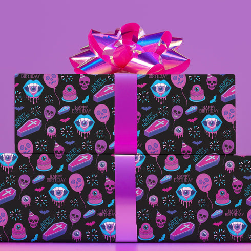 Spooky birthday wrapping paper with neon pink skulls, blue coffins, eyeballs, and bats on black background. Vibrant and gothic design for unique gift presentation.