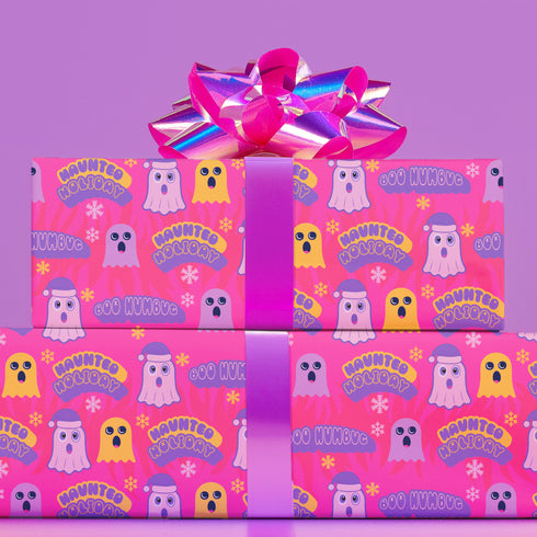 Bright pink christmas wrapping paper covered in cute ghost characters wearing Santa hats, with "Haunted Holiday" and "Boo Humbug" text, and snowflake accents.