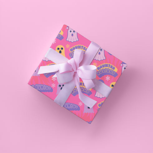 Bright pink christmas wrapping paper covered in cute ghost characters wearing Santa hats, with "Haunted Holiday" and "Boo Humbug" text, and snowflake accents.