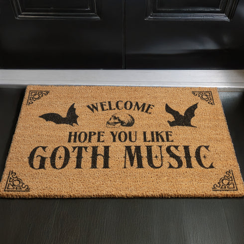 Tan coir doormat featuring "Welcome, Hope You Like Goth Music" in black text, with bat and skull imagery and gothic-style corner decorations.