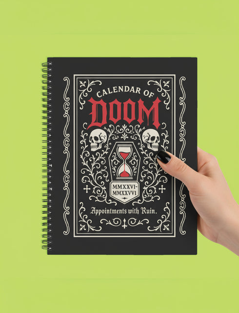 An 8.5 x 11 inch black hardcover spiral planner with a durable satin matte laminated finish. The front cover features a vintage-style white ornamental border, creating a gothic, macabre aesthetic. Inside the frame, the title "Calendar of Doom" is printed in an antique serif font. This undated weekly and monthly agenda is shown with a metal wire-o spiral binding on the right side. The design uses a black, white, and red color scheme, making it a unique piece of dark humor stationery