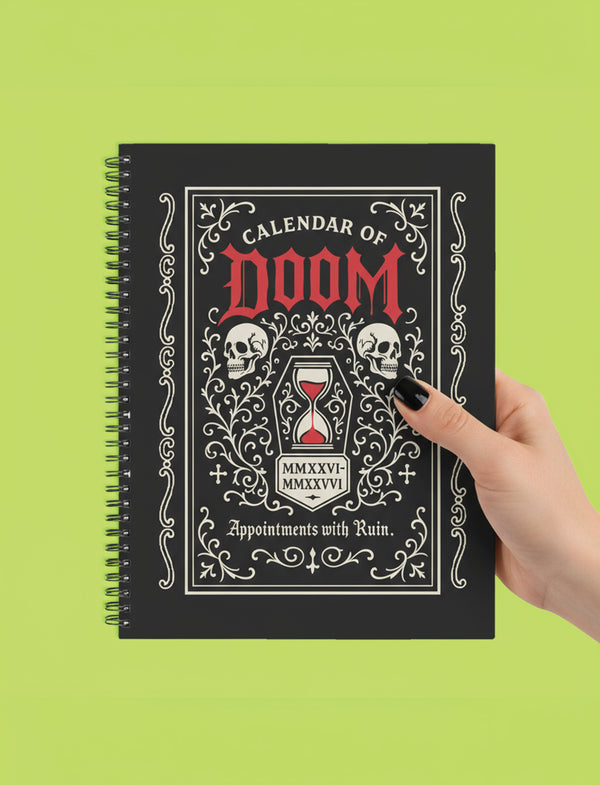 An 8.5 x 11 inch black hardcover spiral planner with a durable satin matte laminated finish. The front cover features a vintage-style white ornamental border, creating a gothic, macabre aesthetic. Inside the frame, the title "Calendar of Doom" is printed in an antique serif font. This undated weekly and monthly agenda is shown with a metal wire-o spiral binding on the right side. The design uses a black, white, and red color scheme, making it a unique piece of dark humor stationery