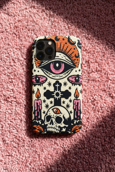 A vertical phone case design featuring a faux crochet texture illusion printed on a cream background. The symmetrical pattern centers on a large black eye with a pink iris and rust-orange sunburst lashes at the top. Below the eye is a black cross surrounded by small black stars. The bottom features a skull with a third rust-orange eye on its forehead. Flanking the skull are two candles with orange flames and rust-colored leaves. The design mimics the look of stitched yarn but is a 2d print.
