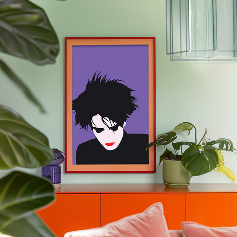 A minimalist portrait of Robert Smith from The Cure against a purple background. The image shows his signature wild black hair, pale white face, and iconic red lipstick in a simplified, high-contrast style. His head is slightly tilted downward in his characteristic brooding pose.