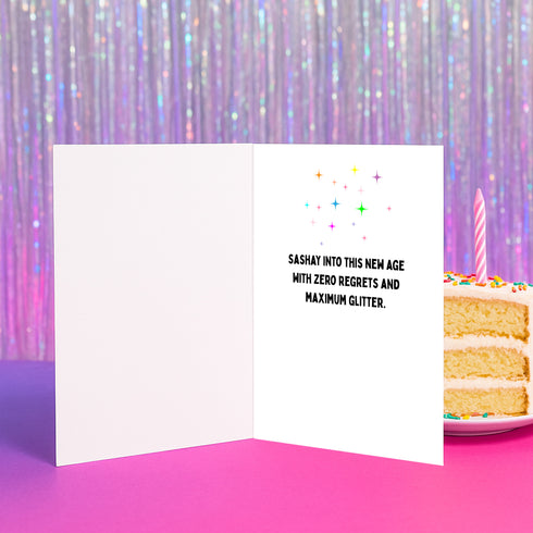 5x7 inch birthday greeting card with a yellow background featuring the phrase “Have the Gayest Day Ever” in bold pink text, a rainbow birthday cake with candles spelling “SLAY,” and two green frogs wearing colorful platform boots. Card includes confetti details and a white envelope. Printed on 120lb silk cover stock. The inside message reads: “Sashay into this new age with zero regrets and maximum glitter.”
