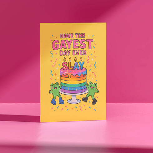5x7 inch birthday greeting card with a yellow background featuring the phrase “Have the Gayest Day Ever” in bold pink text, a rainbow birthday cake with candles spelling “SLAY,” and two green frogs wearing colorful platform boots. Card includes confetti details and a white envelope. Printed on 120lb silk cover stock. The inside message reads: “Sashay into this new age with zero regrets and maximum glitter.”