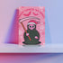 Quirky Christmas card featuring grim reaper in Santa hat. Pink background with bats, snowflakes, skull motifs. Text reads 'Grave Tidings We Bring'. Humorous blend of holiday cheer and gothic aesthetic. Perfect for alternative Christmas greetings.
