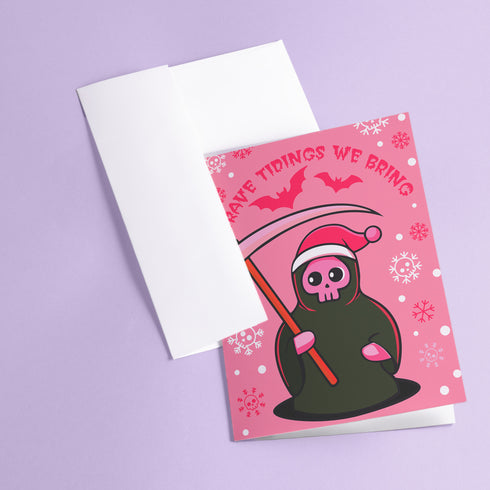 Quirky Christmas card featuring grim reaper in Santa hat. Pink background with bats, snowflakes, skull motifs. Text reads 'Grave Tidings We Bring'. Humorous blend of holiday cheer and gothic aesthetic. Perfect for alternative Christmas greetings.