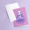 Birthday card featuring a cute cartoon grim reaper holding a birthday cake on pink background. The reaper wears a purple cloak and has a white skull face. It's carrying a small purple cake with three lit candles. The reaper's cloak drips like melting icing at the bottom. Ideal for Halloween birthdays or gothic-themed celebrations. Inside greeting: "Hope your B-day is spooky AF and sweet as cake!"