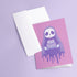 Birthday card featuring a cute cartoon grim reaper holding a birthday cake on pink background. The reaper wears a purple cloak and has a white skull face. It's carrying a small purple cake with three lit candles. The reaper's cloak drips like melting icing at the bottom. Ideal for Halloween birthdays or gothic-themed celebrations. Inside greeting: "Hope your B-day is spooky AF and sweet as cake!"