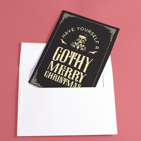 A black holiday card featuring gothic-style text that reads "Have Yourself a Gothy Merry Christmas." The design includes a skull wearing a Santa hat, bats, and ornate decorative borders, combining a dark, spooky aesthetic with festive holiday elements.