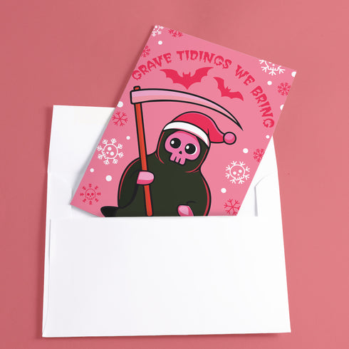 Quirky Christmas card featuring grim reaper in Santa hat. Pink background with bats, snowflakes, skull motifs. Text reads 'Grave Tidings We Bring'. Humorous blend of holiday cheer and gothic aesthetic. Perfect for alternative Christmas greetings.