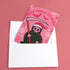 Quirky Christmas card featuring grim reaper in Santa hat. Pink background with bats, snowflakes, skull motifs. Text reads 'Grave Tidings We Bring'. Humorous blend of holiday cheer and gothic aesthetic. Perfect for alternative Christmas greetings.