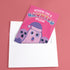 Holiday card with pink background featuring cartoon ghosts. Main ghost wears purple Santa hat. Text reads "WISHING YOU A HAUNTED HOLIDAY" in colorful, playful font. Overall cute and spooky design blending Halloween and Christmas themes. Inside message: "Eat, Drink, and Be Scary.