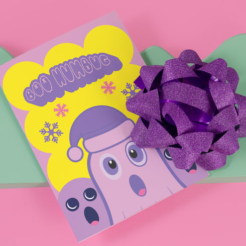 Christmas card with a playful ghost theme. Central cute pink ghost wearing a purple Santa hat, flanked by two smaller purple ghosts. Yellow background with snowflakes. Text reads "Boo HUMBUG" in purple bubble letters. Blends Christmas and Halloween elements for a unique holiday greeting. Inside message: "May your Christmas be filled with delight, not fright.
