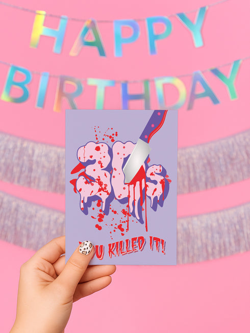 A 5x7 folded birthday card featuring a horror-themed design. The front shows the number “30s” in pink, gooey lettering with blood splatters and a dripping butcher knife through it. The bottom reads “YOU KILLED IT!” in red, jagged font. The inside right panel reads “HERE’S TO THE NEXT VICTIM: YOUR FORTIES!” with red blood dripping from the top. Card is printed on smooth white cardstock and comes with a white envelope. Designed for a milestone 40th birthday.