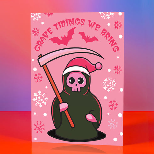Quirky Christmas card featuring grim reaper in Santa hat. Pink background with bats, snowflakes, skull motifs. Text reads 'Grave Tidings We Bring'. Humorous blend of holiday cheer and gothic aesthetic. Perfect for alternative Christmas greetings.