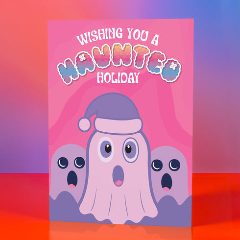 Holiday card with pink background featuring cartoon ghosts. Main ghost wears purple Santa hat. Text reads "WISHING YOU A HAUNTED HOLIDAY" in colorful, playful font. Overall cute and spooky design blending Halloween and Christmas themes. Inside message: "Eat, Drink, and Be Scary.
