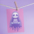 Birthday card featuring a cute cartoon grim reaper holding a birthday cake on pink background. The reaper wears a purple cloak and has a white skull face. It's carrying a small purple cake with three lit candles. The reaper's cloak drips like melting icing at the bottom. Ideal for Halloween birthdays or gothic-themed celebrations. Inside greeting: "Hope your B-day is spooky AF and sweet as cake!"