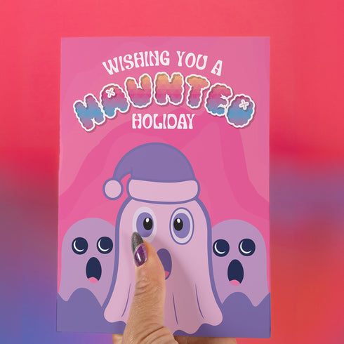 Holiday card with pink background featuring cartoon ghosts. Main ghost wears purple Santa hat. Text reads "WISHING YOU A HAUNTED HOLIDAY" in colorful, playful font. Overall cute and spooky design blending Halloween and Christmas themes. Inside message: "Eat, Drink, and Be Scary.