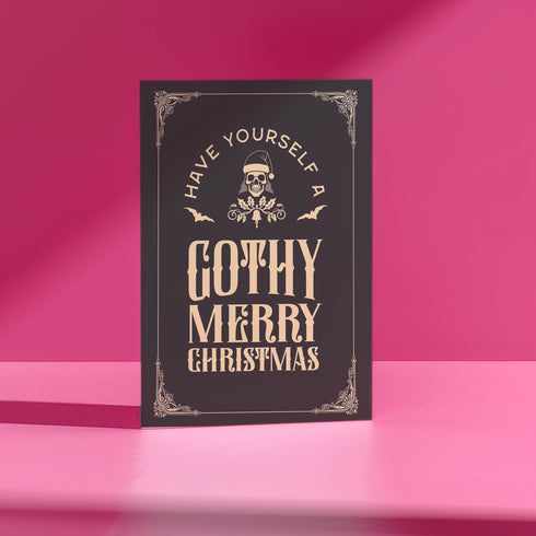 A black holiday card featuring gothic-style text that reads "Have Yourself a Gothy Merry Christmas." The design includes a skull wearing a Santa hat, bats, and ornate decorative borders, combining a dark, spooky aesthetic with festive holiday elements.