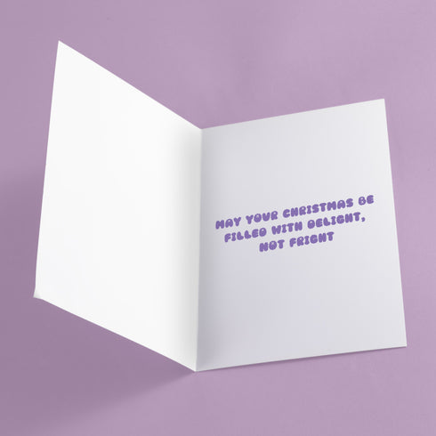 Christmas card with a playful ghost theme. Central cute pink ghost wearing a purple Santa hat, flanked by two smaller purple ghosts. Yellow background with snowflakes. Text reads "Boo HUMBUG" in purple bubble letters. Blends Christmas and Halloween elements for a unique holiday greeting. Inside message: "May your Christmas be filled with delight, not fright.