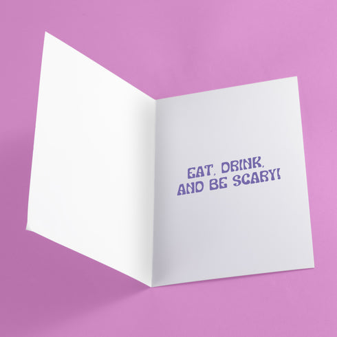Holiday card with pink background featuring cartoon ghosts. Main ghost wears purple Santa hat. Text reads "WISHING YOU A HAUNTED HOLIDAY" in colorful, playful font. Overall cute and spooky design blending Halloween and Christmas themes. Inside message: "Eat, Drink, and Be Scary.