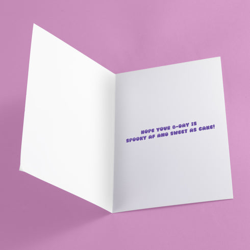 Birthday card featuring a cute cartoon grim reaper holding a birthday cake on pink background. The reaper wears a purple cloak and has a white skull face. It's carrying a small purple cake with three lit candles. The reaper's cloak drips like melting icing at the bottom. Ideal for Halloween birthdays or gothic-themed celebrations. Inside greeting: "Hope your B-day is spooky AF and sweet as cake!"