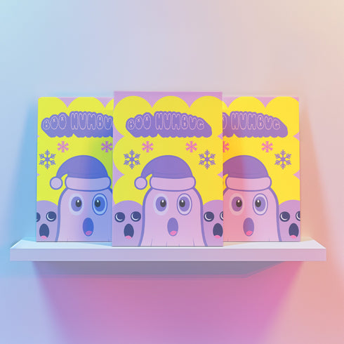 Christmas card with a playful ghost theme. Central cute pink ghost wearing a purple Santa hat, flanked by two smaller purple ghosts. Yellow background with snowflakes. Text reads "Boo HUMBUG" in purple bubble letters. Blends Christmas and Halloween elements for a unique holiday greeting. Inside message: "May your Christmas be filled with delight, not fright.