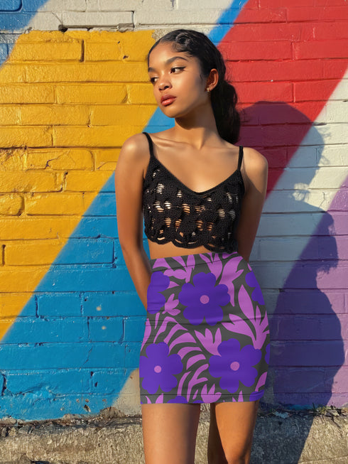 High waisted mini skirt with bold purple and pink floral print in a vibrant, maximalist style. Features a sculpted, body-hugging fit with a 1.5-inch elastic waistband that sits comfortably at the natural waist. Made from eco polyester and spandex blend that is stretchy, quick-drying, odor-resistant, and includes UPF 50 UV protection. Available in standard or glittery metallic finish in sizes S to XL.