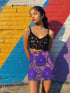 High waisted mini skirt with bold purple and pink floral print in a vibrant, maximalist style. Features a sculpted, body-hugging fit with a 1.5-inch elastic waistband that sits comfortably at the natural waist. Made from eco polyester and spandex blend that is stretchy, quick-drying, odor-resistant, and includes UPF 50 UV protection. Available in standard or glittery metallic finish in sizes S to XL.