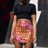 Form-fitting mini skirt featuring a vibrant, retro-inspired maximalist pattern. The design showcases a diagonal hot pink band filled with white and yellow daisies, contrasting against a bold background of wavy, abstract red and yellow flame-like stripes. The bottom edge includes curved color blocks of green and orange. Made of a smooth, stretchy fabric with a mid-rise elastic waistband, hitting at mid-thigh. Available in both a matte black-light reactive finish and a metallic glitter finish.