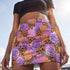 A vibrant, curve-hugging bodycon mini skirt featuring a maximalist mix of orange and purple checkerboard, black leopard print, and realistic rose florals in purple and orange tones. The high-waisted, mid-thigh cut is designed for a confident fit. Made from a durable performance knit fabric with two finish options: a signature UV reactive version that glows under blacklight for festivals and a dazzling glitter knit with reflective silver foil for a party-ready shimmer.