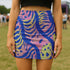 High-waisted mini skirt with a vibrant pastel tiger stripe pattern in electric blue, soft pink, yellow, and violet. The bodycon silhouette hugs curves with a comfy elastic waistband and stretch fabric. Available in smooth performance fabric or glitter finish. A maximalist fashion piece for festivals, summer outfits, and ravewear.