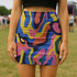Psychedelic high waisted mini skirt for women featuring a trippy swirl print in yellow, pink, purple, and blue. Fitted bodycon silhouette with 1.5” elastic waistband, made from eco-friendly polyester and spandex blend. Available in sizes S to XL with built-in UPF 50 sun protection and odor-resistant, quick-dry performance fabric. Festival-ready, rave-approved, and styled for bold streetwear and summer outfits.
