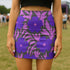 High waisted mini skirt with bold purple and pink floral print in a vibrant, maximalist style. Features a sculpted, body-hugging fit with a 1.5-inch elastic waistband that sits comfortably at the natural waist. Made from eco polyester and spandex blend that is stretchy, quick-drying, odor-resistant, and includes UPF 50 UV protection. Available in standard or glittery metallic finish in sizes S to XL.