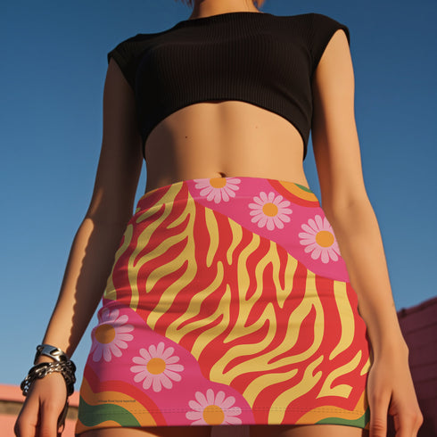 Form-fitting mini skirt featuring a vibrant, retro-inspired maximalist pattern. The design showcases a diagonal hot pink band filled with white and yellow daisies, contrasting against a bold background of wavy, abstract red and yellow flame-like stripes. The bottom edge includes curved color blocks of green and orange. Made of a smooth, stretchy fabric with a mid-rise elastic waistband, hitting at mid-thigh. Available in both a matte black-light reactive finish and a metallic glitter finish.